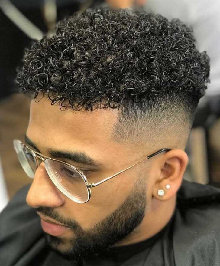 Man with curly short hair and glasses sitting in barbershop.