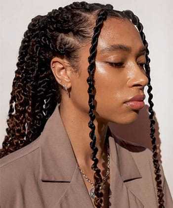 Woman with braided hair, wearing a tan blazer, looking to the side against a plain background.
