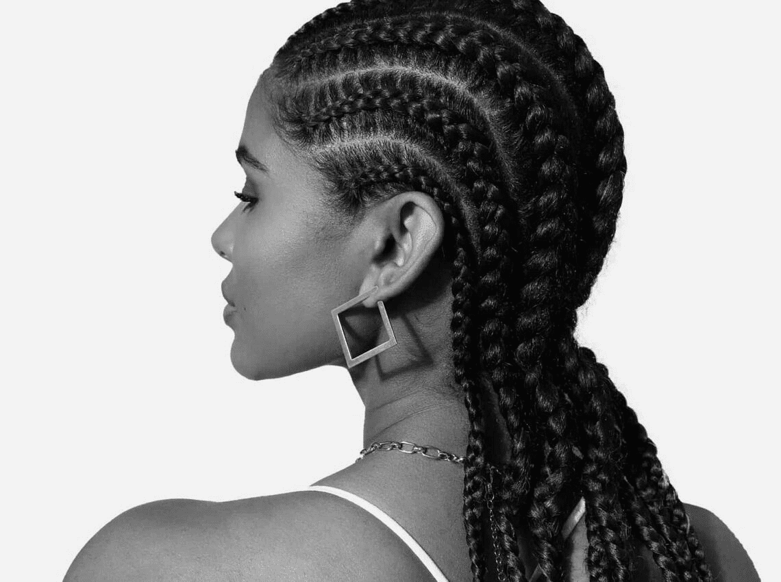 Woman with braided cornrows and geometric earrings, viewed from the side.