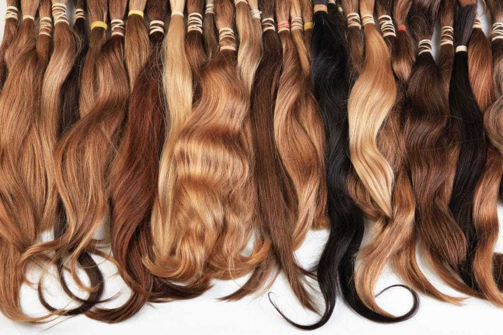 Various shades of hair extensions arranged in rows, ranging from light brown to dark brown and black.