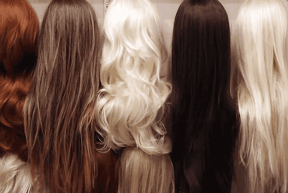 Rows of wigs in various shades from red and brown to blonde and black, displayed on stands.