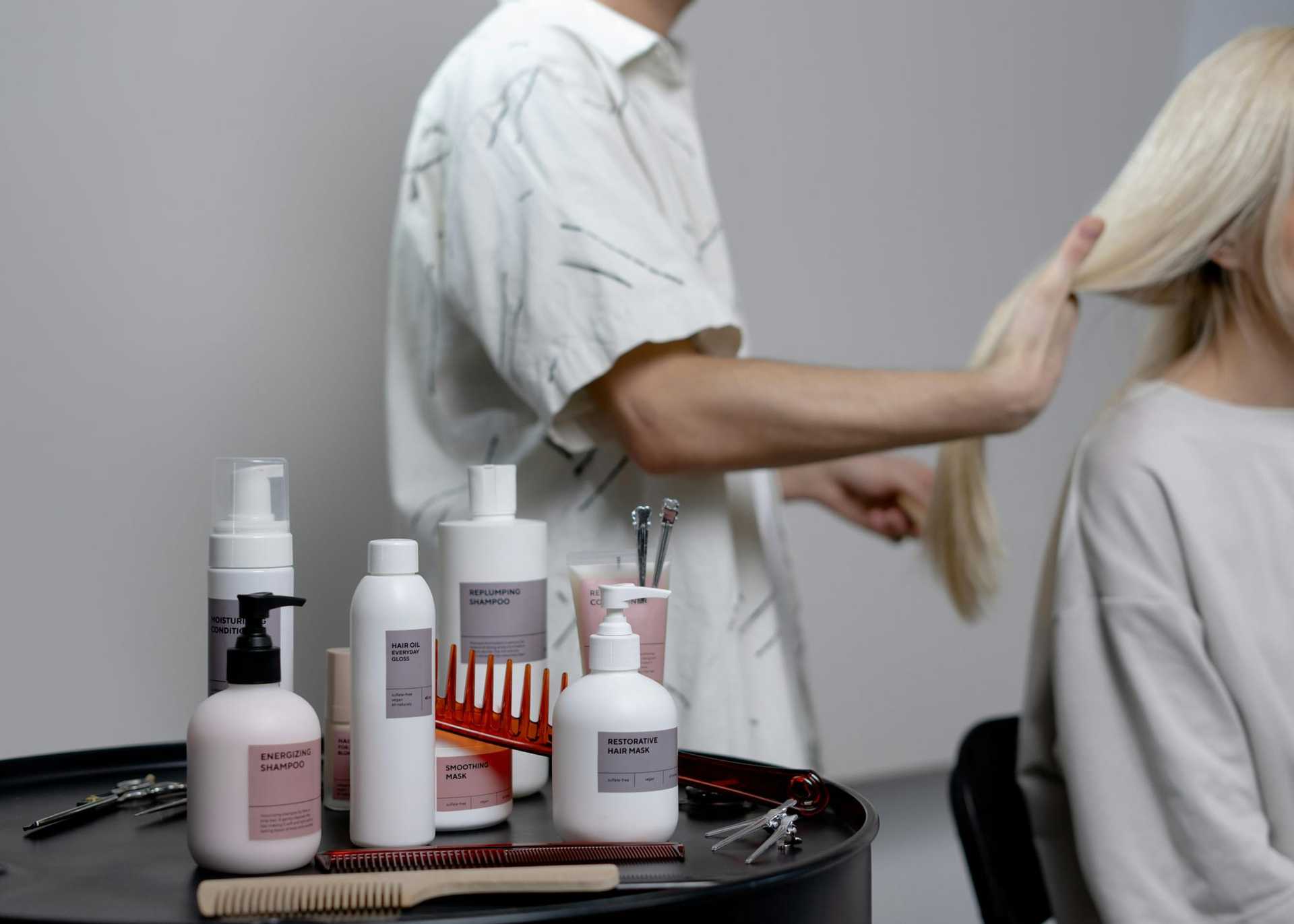 Hair products on a table while a stylist works on a client's blonde hair in a salon.