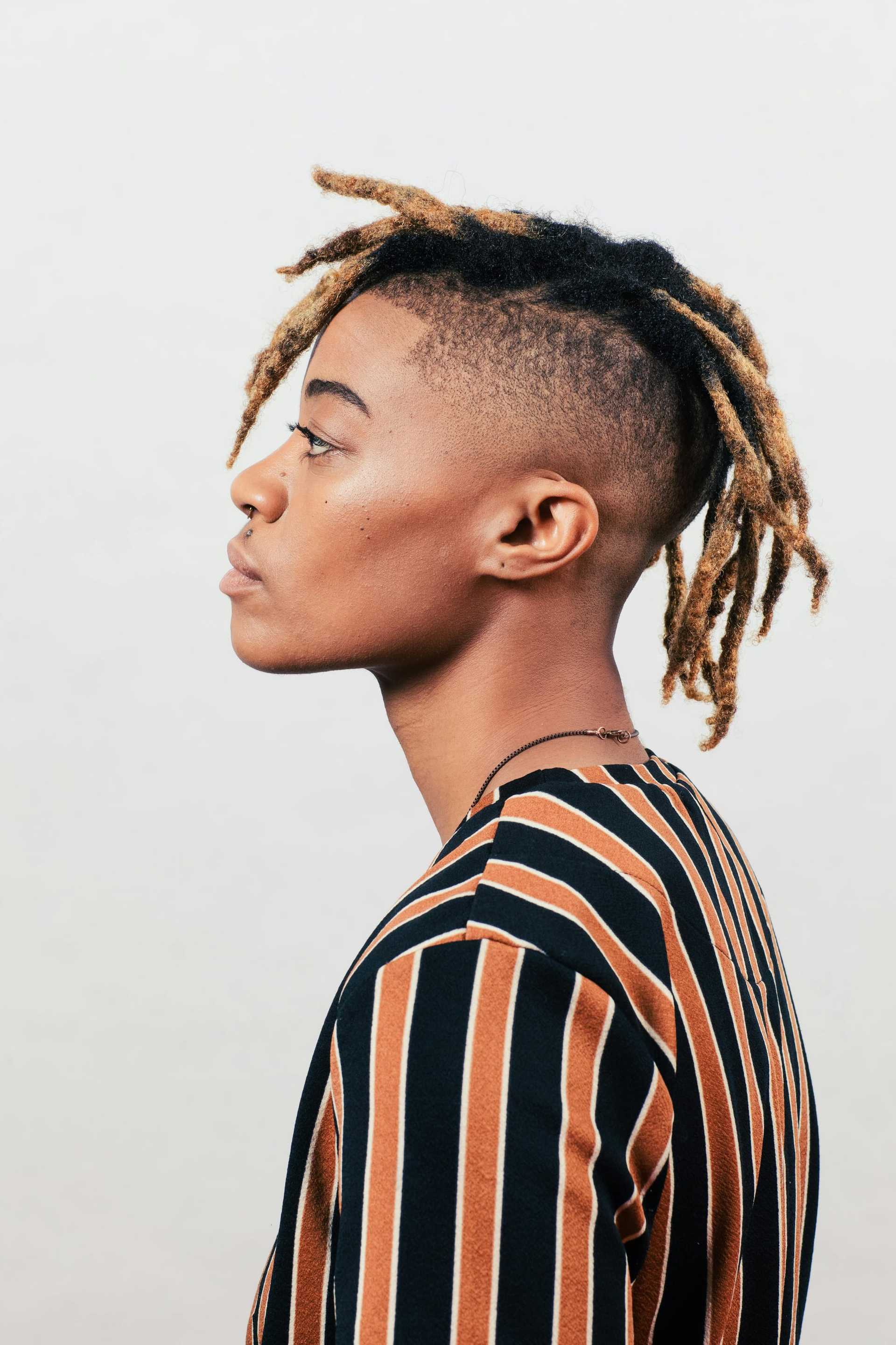 Person with dreadlocks and a striped shirt looking to the left.