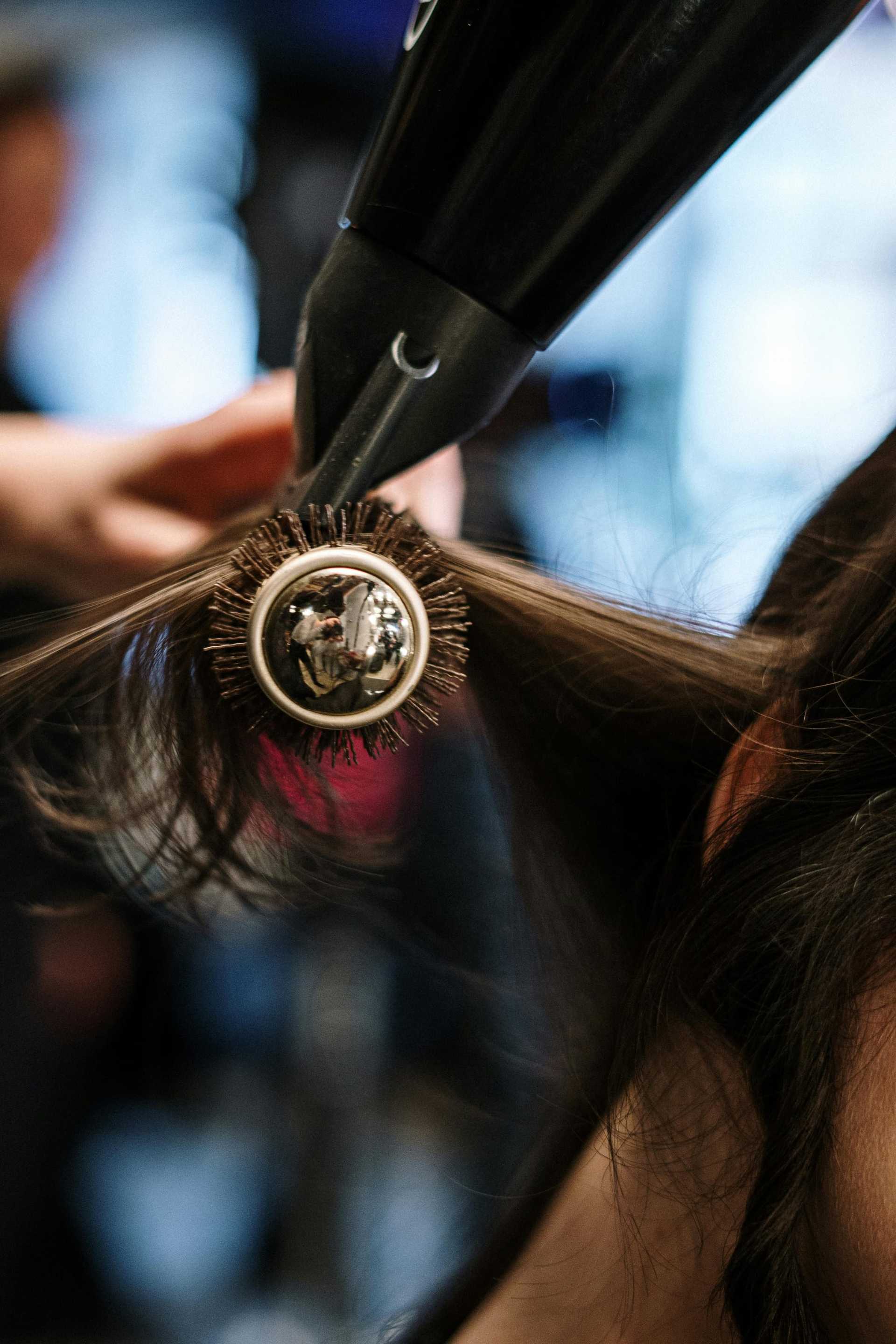 Hair being styled with a round brush and hair dryer in a salon.